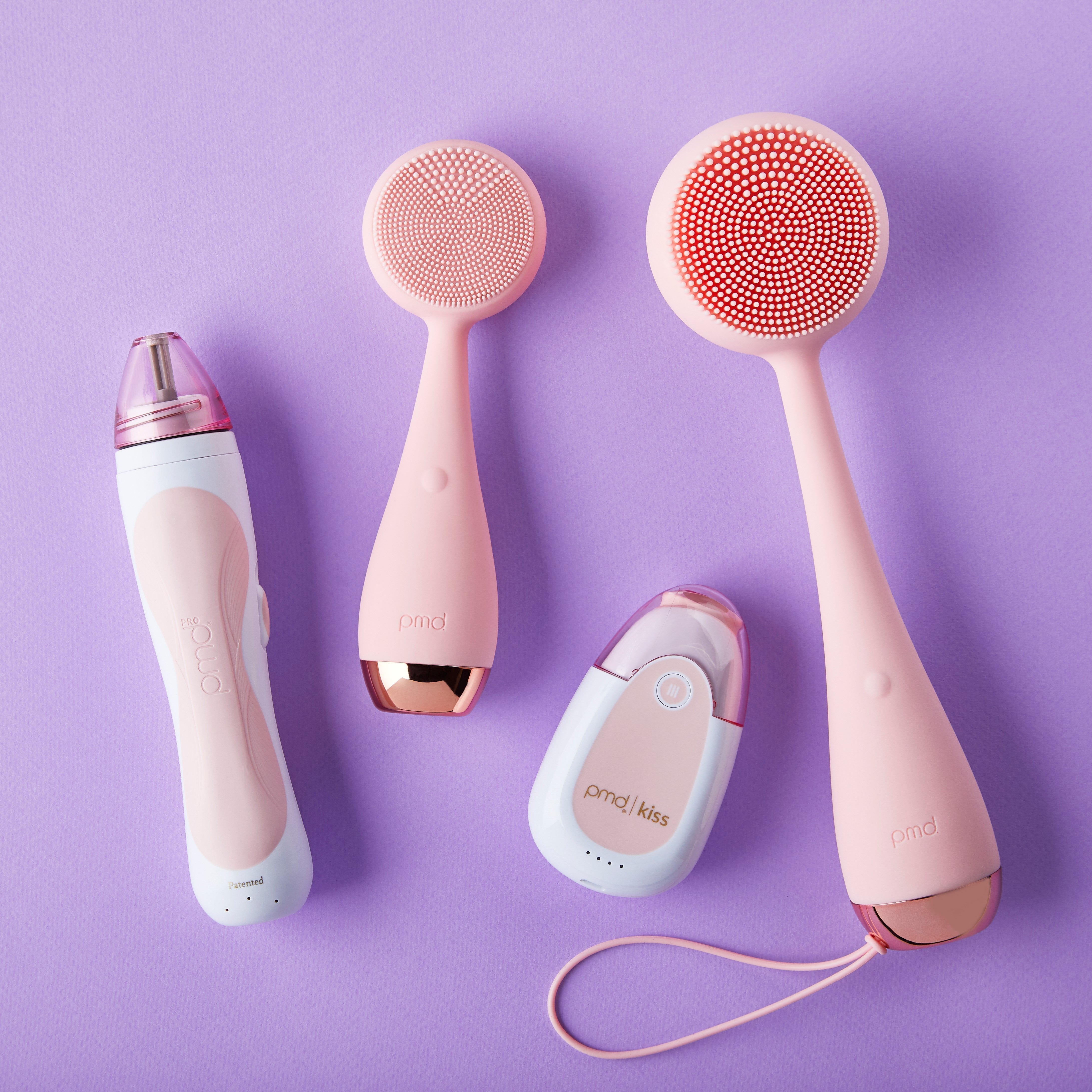 Flatlay of PMD Beauty devices — PMD Kiss lip plumping system, PMD Clean Body, PMD Clean facial cleansing device, and PMD Personal Microderm — highlighting PMD Beauty’s complete at-home skincare and anti-aging routine.