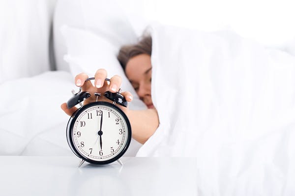 Woman reaching out from under covers to turn off alarm clock