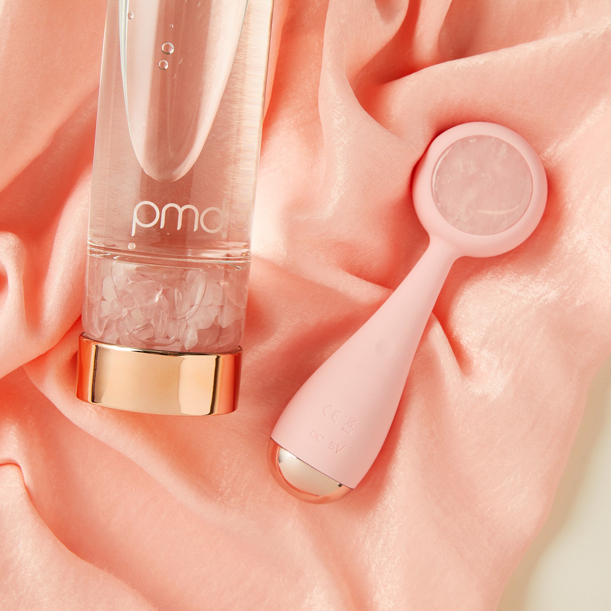 5012-RQ?Close up of PMD Aqua Rose Quartz Water Bottle and PMD Clean Pro RQ on pink satin fabric