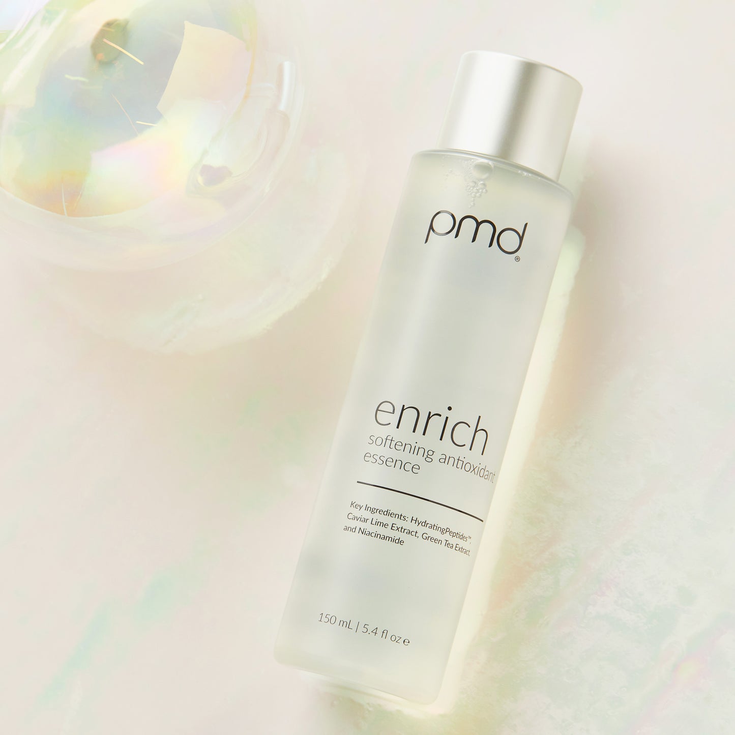 Enrich Softening Antioxidant Essence laying down next to clear globe