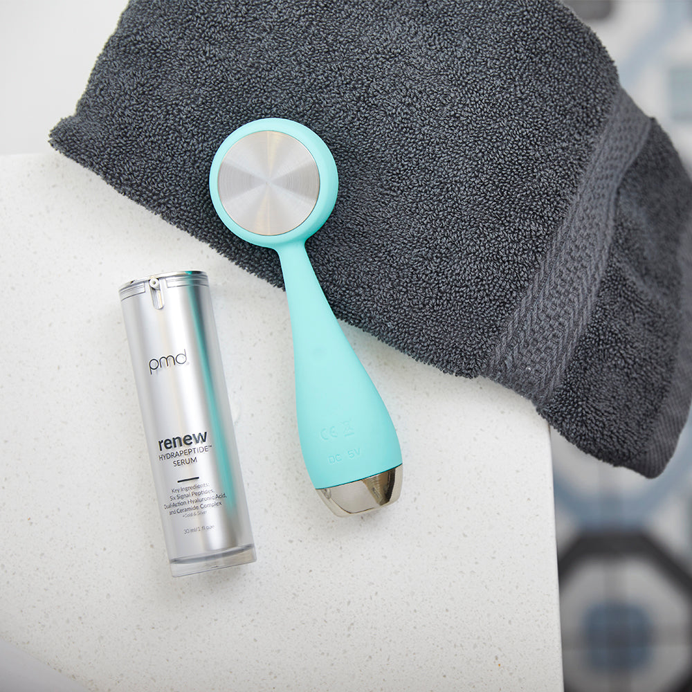 1031-RENEW?renew HydratingPeptides™ Serum on counter with PMD Clean Pro in teal and towel